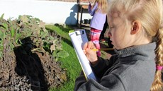 Young girl outside in a garden writing on a clipboard