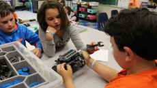 Young girl looking at a robotics part held by a young boy in a classroom