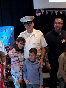 An elderly man in a white Navy uniform with two young children in front of him