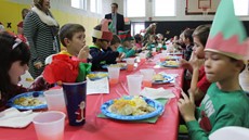 A long table with young students sitting on each side with plates of food in front of them