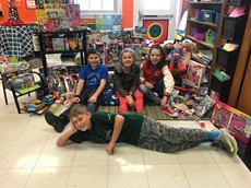 Elementary students pose with bags of toys in a classroom