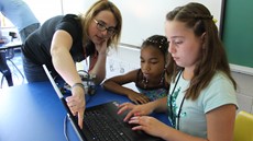 Teacher pointing at a computer screen with two students looking on