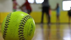 Softball in focus in foreground with children out of focus in background