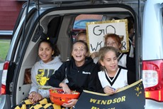 Three smiling young girls in Windsor clothing sitting in open hatch of SUV 