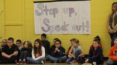 Children sitting underneath a sign reading, "Step up, speak out"