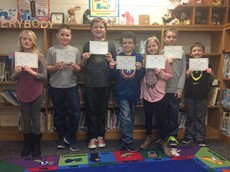 Seven students holding up certificates, standing in front of bookshelves