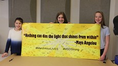 Three female middle school students hold up a banner