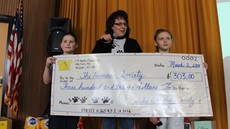 Two young students and an adult holding a big check