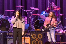 One student holding a microphone and another with a guitar on stage