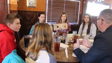 Five students and Jason Andrews seated at a table in a restaurant