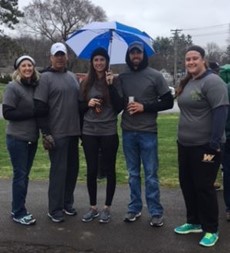 Five people standing in a park, with one holding an umbrella