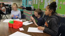 Three young students working at a desk in a classroom