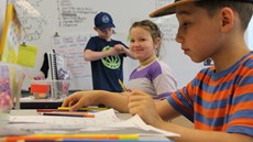 A young boy working at a desk with a smiling girl next to him