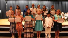 Two rows of fifth grade students standing on risers in front of a stage