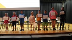 Children standing on stage holding certificates