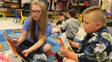 A girl and boy sitting on a rug reading