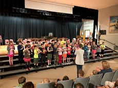 Rows of young children standing in the front of an auditorium