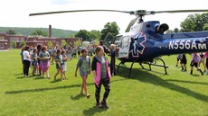 A line of children walking around a helicopter in a field