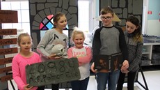 Five children standing in front of a background of painted cardboard walls