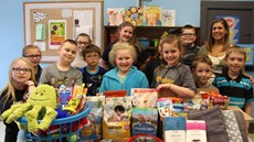 12 children and an adult stand by a table with pet toys and food on it