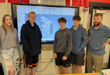 A girl, three boys, and an adult standing in front of a screen