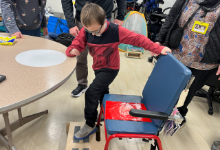 Boy standing on a stool by a chair