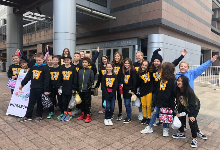 A group of two dozen young students pose for a picture outside a building