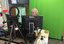 Eileen Mulcahy at a desk in front of a green screen