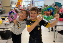 Two smiling children holding up art work