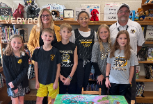 Two adults and a group of children standing by a table