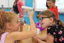 Two young girls looking at a bug in a jar