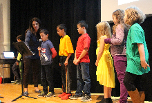 Six young children and a woman standing on a stage