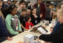 A group of young girls standing around a table in a crowded room