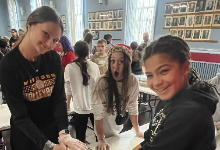 Three 7th grade girls standing over a table