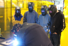 Four people in welding masks looking at welder