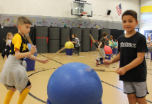 Two boys with drum sticks standing next to a medicine ball