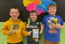 Three young boys holding trophies and a plaque