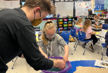 Man and girl standing over a bucket in a classroom