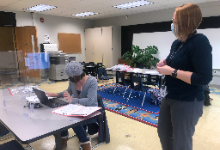 One woman sitting at a desk, another one standing