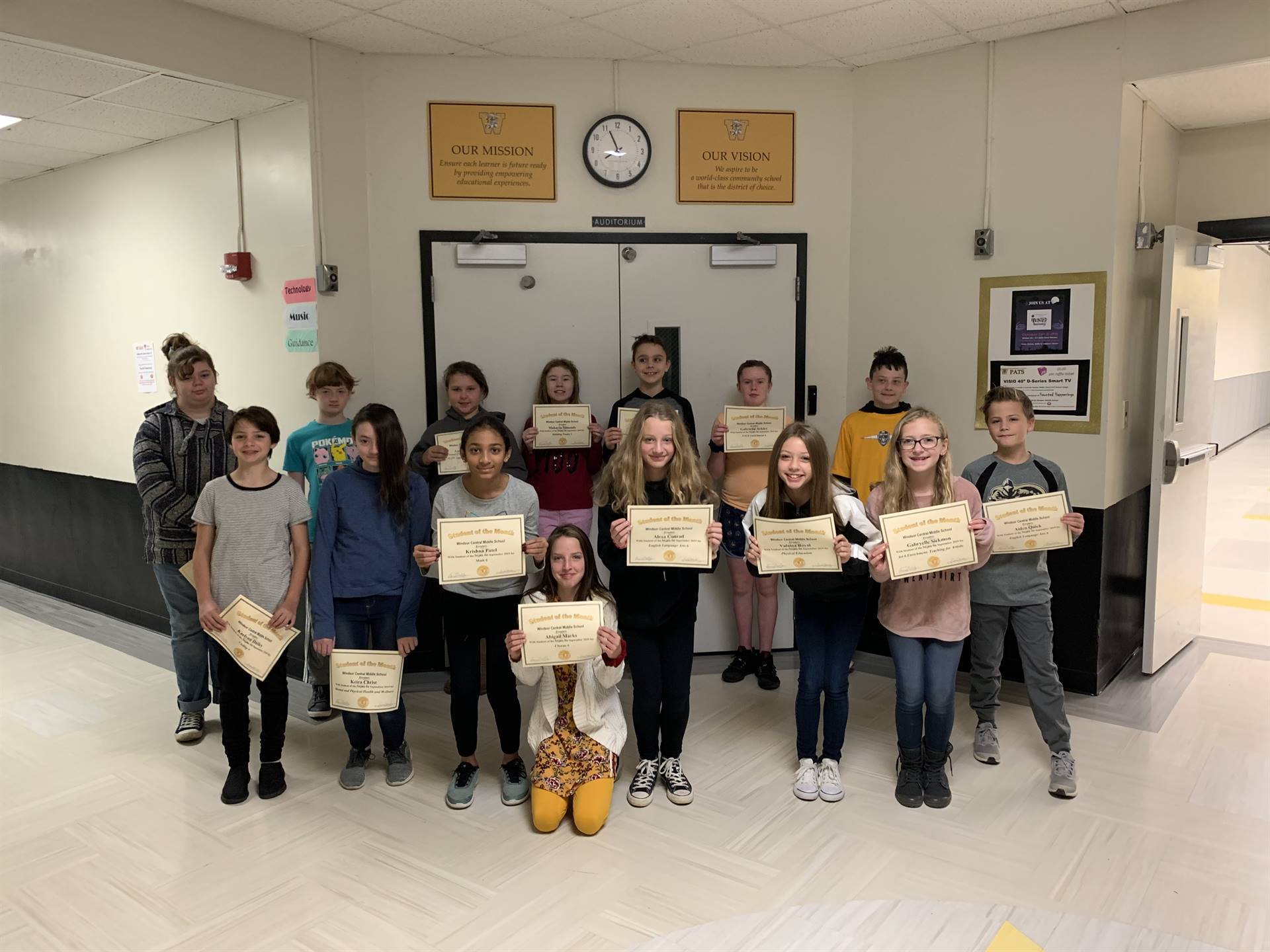 15 6th graders holding certificates in a hallway