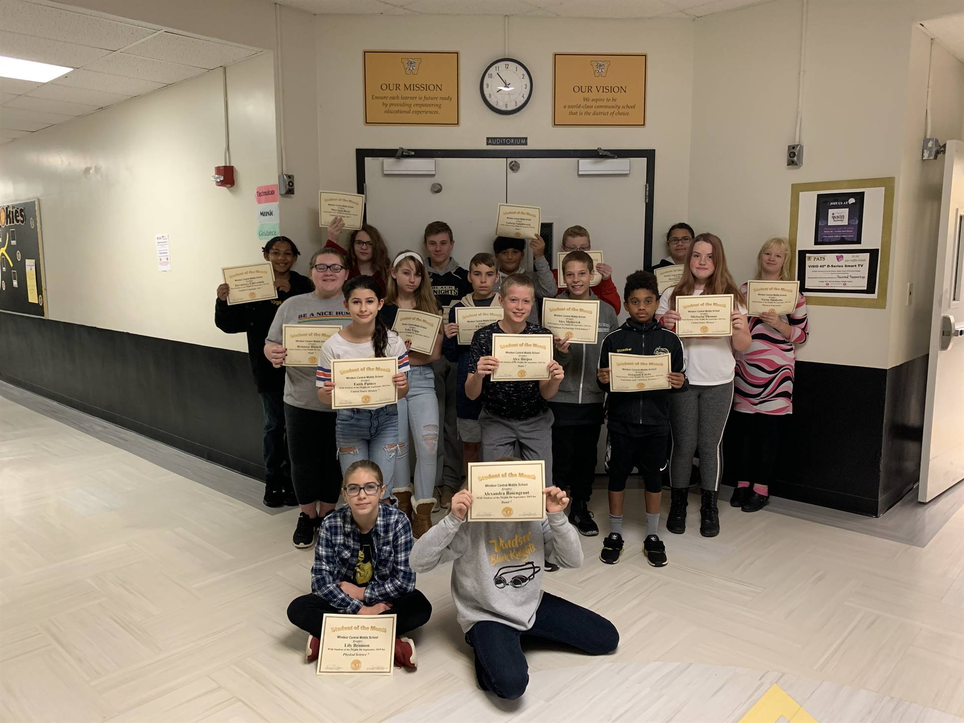 17 7th graders holding certificates in a hallway