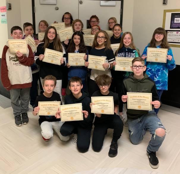 16 8th graders holding certificates in a hallway