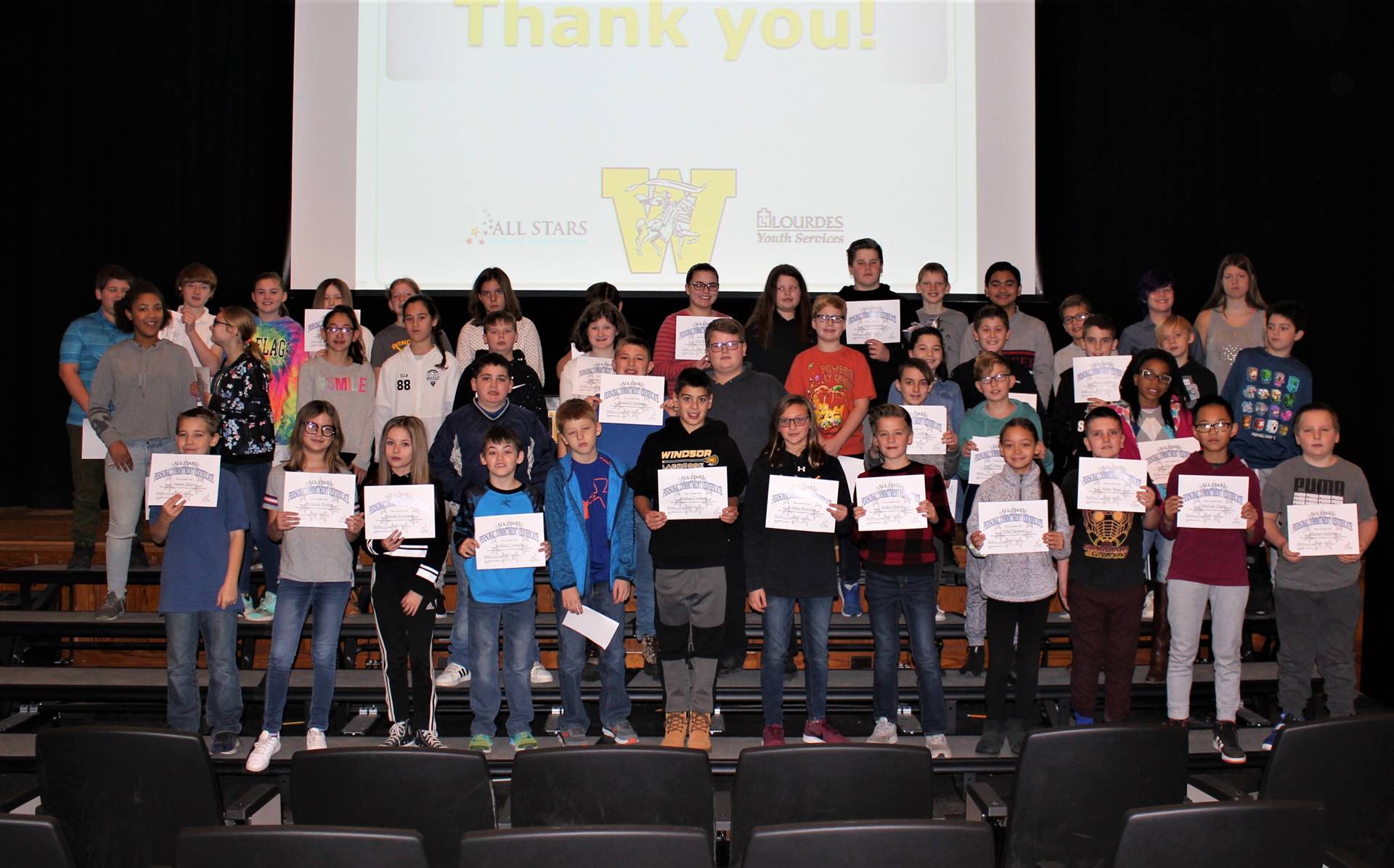 Four rows of students on a stage holding certificates