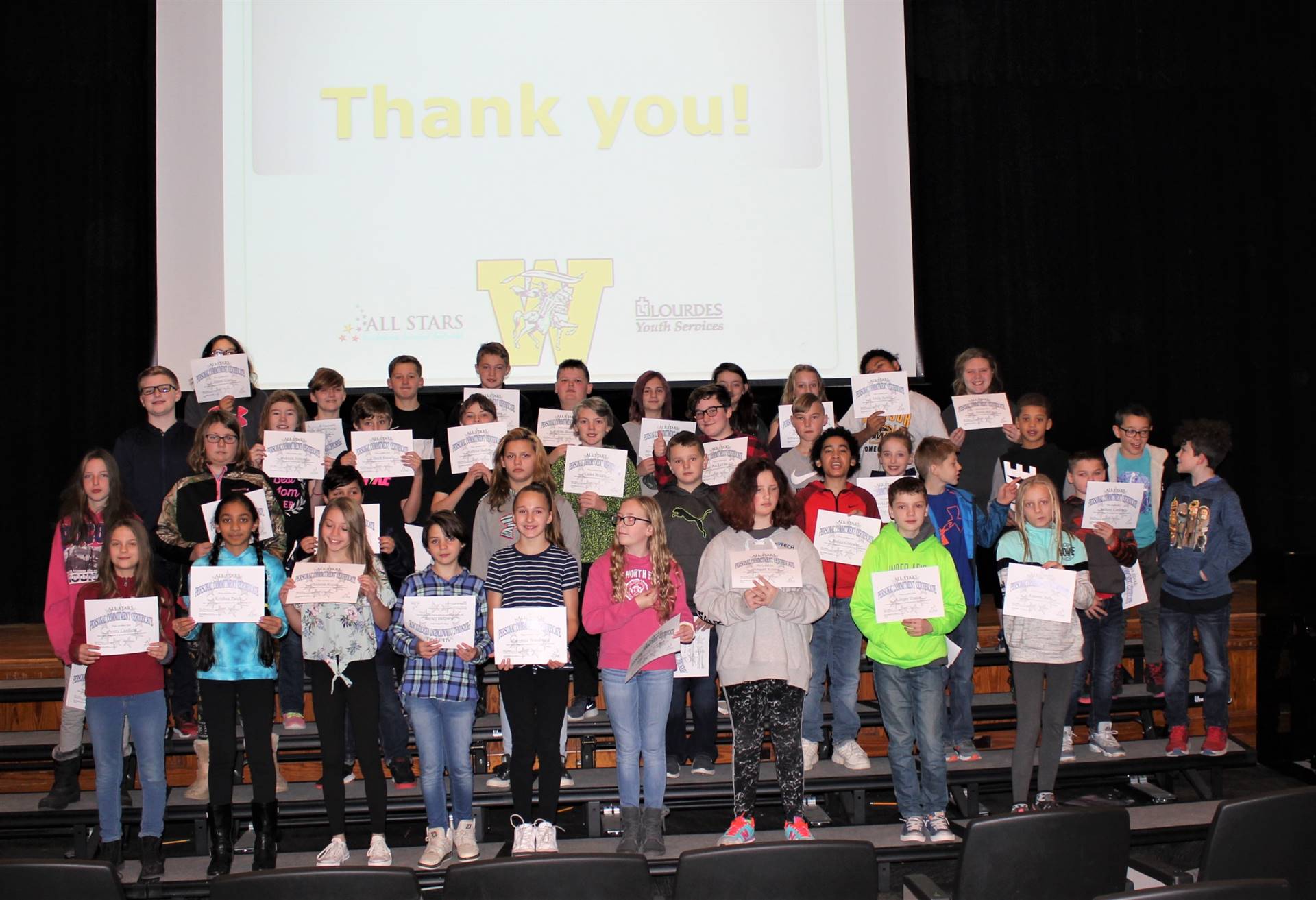 Four rows of students on a stage holding certificates