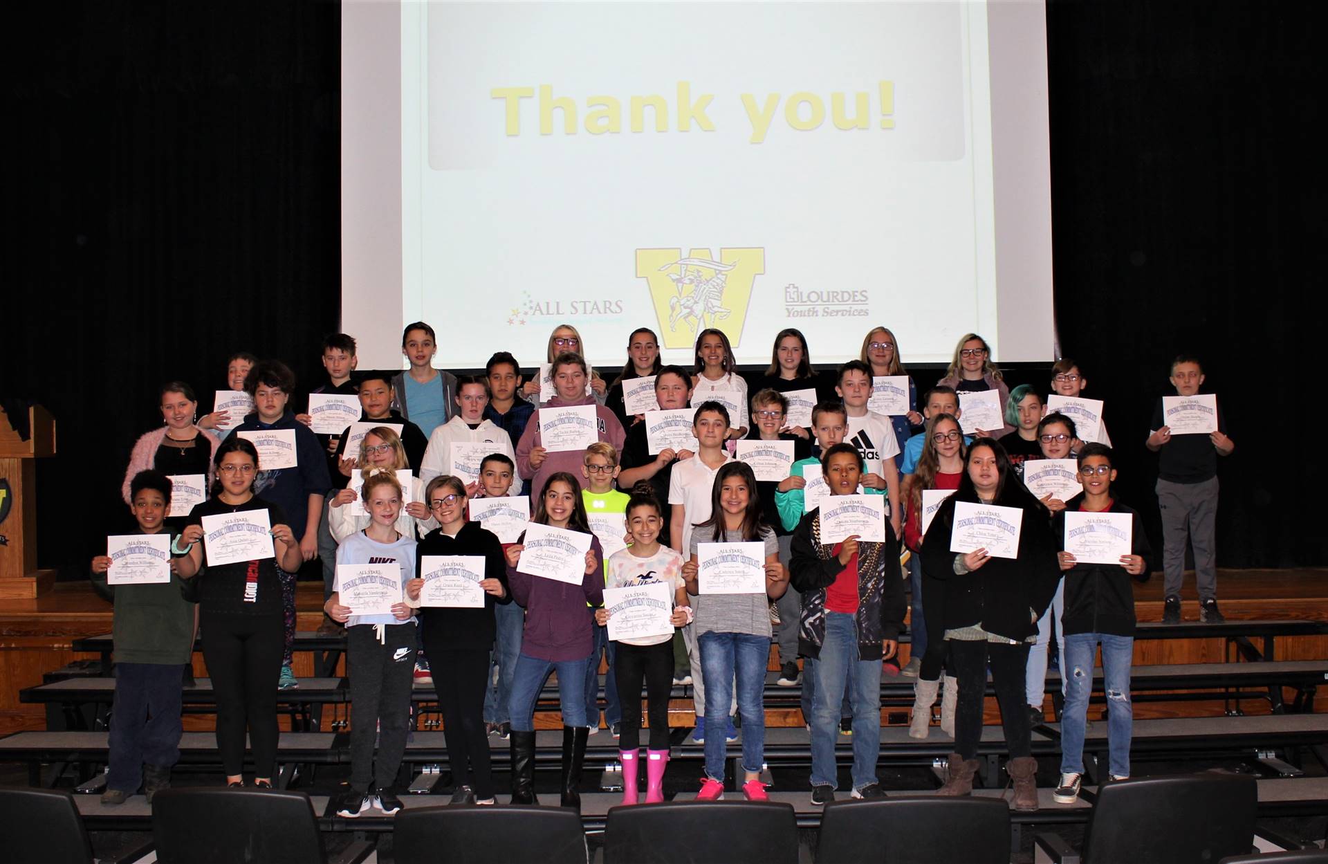 Four rows of students on a stage holding certificates
