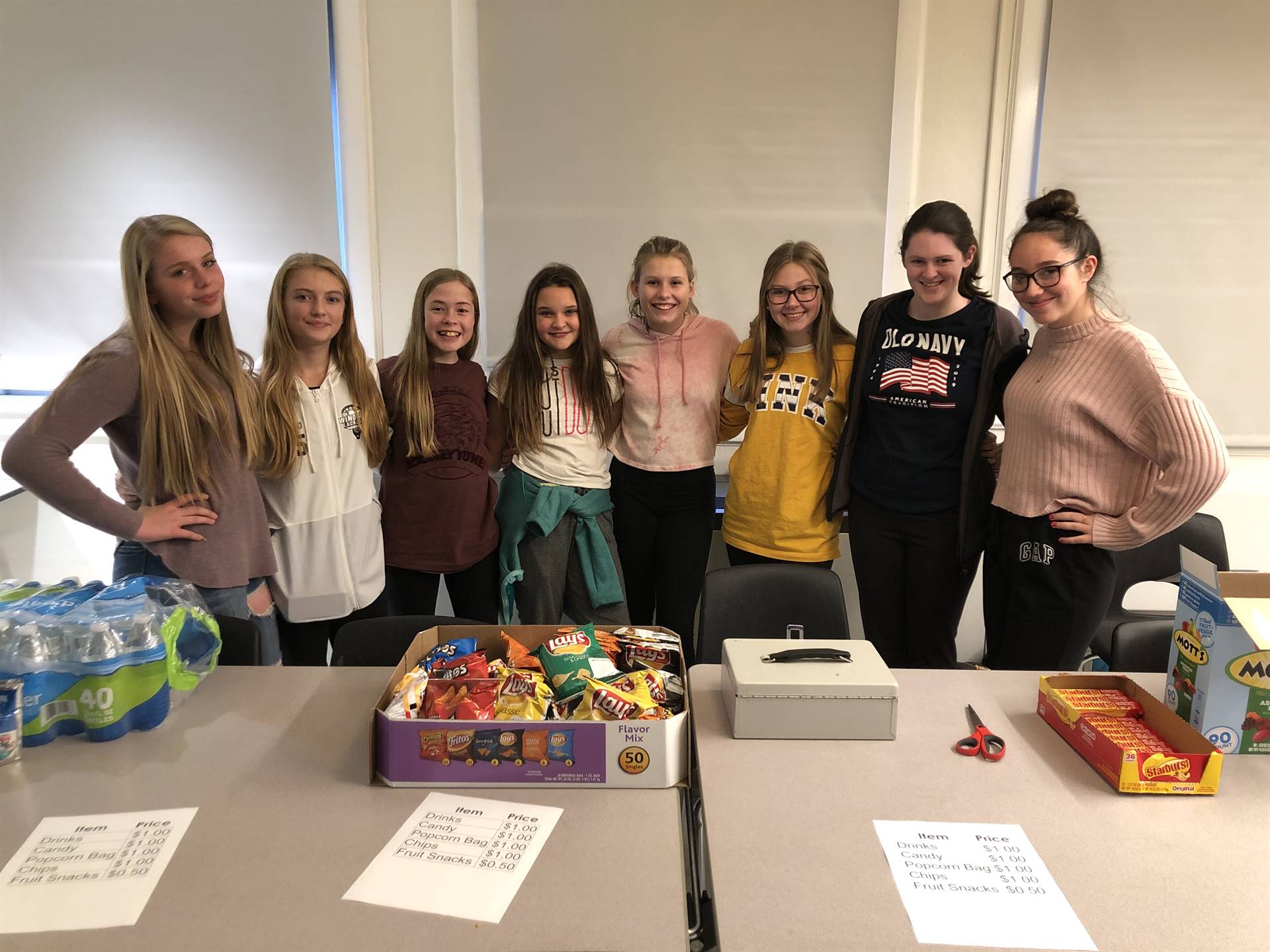 Eight girls standing next to each other behind two tables