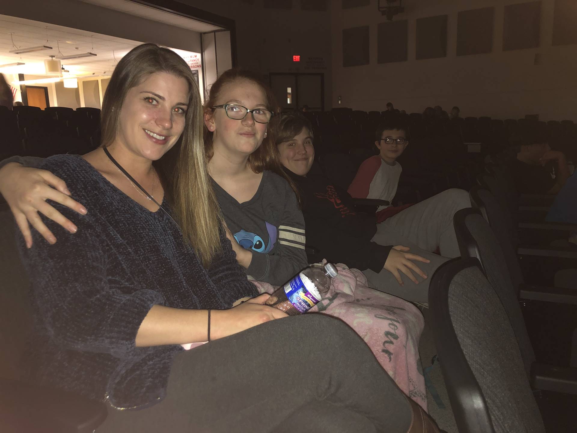 A group of middle school students sitting in auditorium seats with a woman