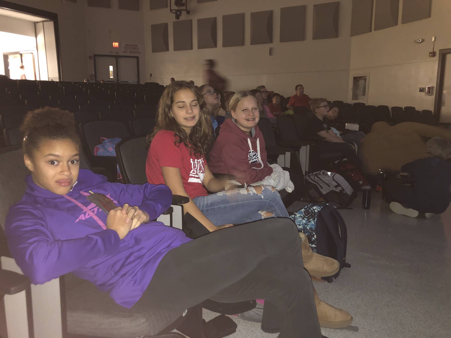 A group of middle school students sitting in auditorium seats