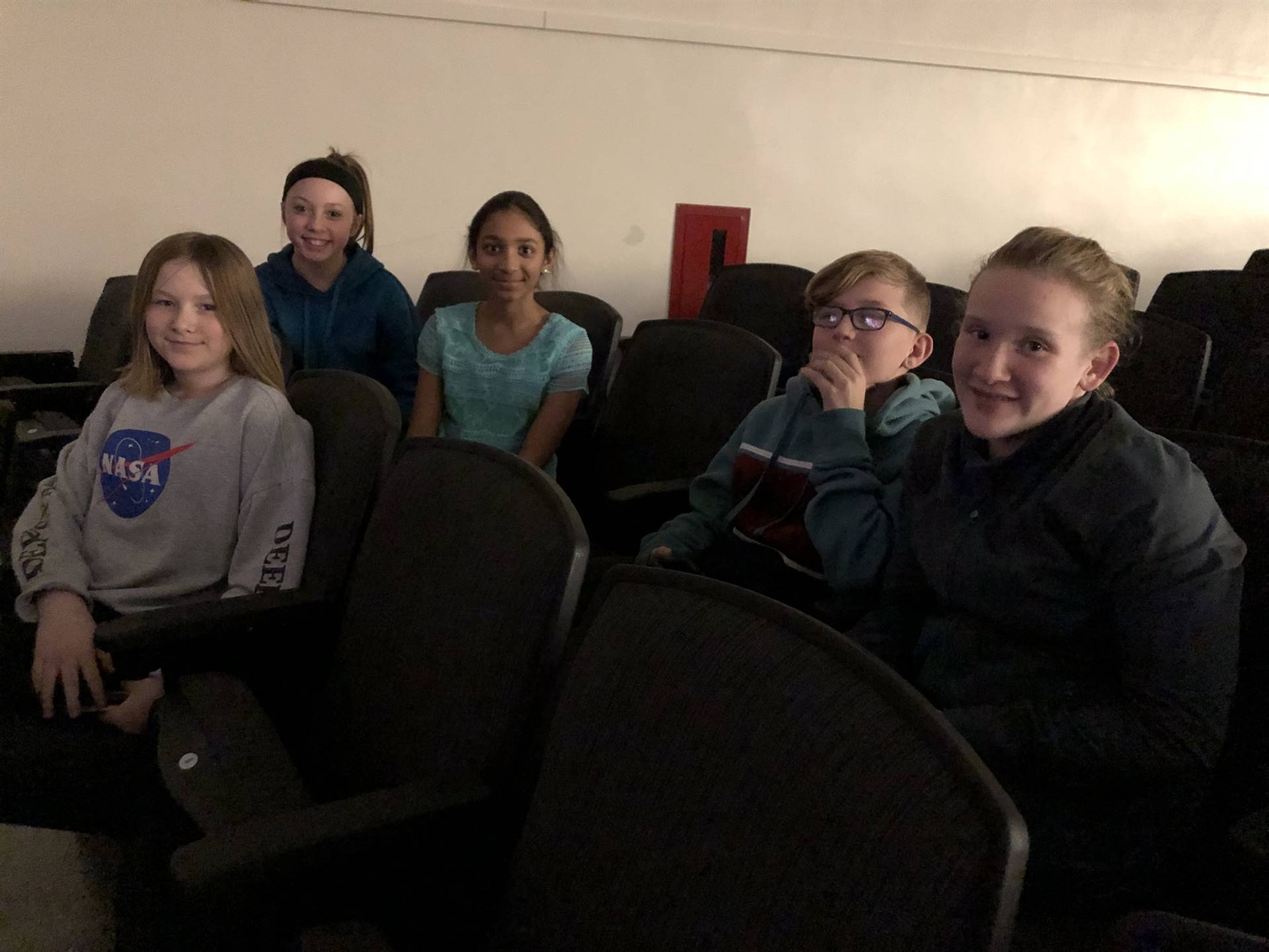 A group of middle school students sitting in auditorium seats