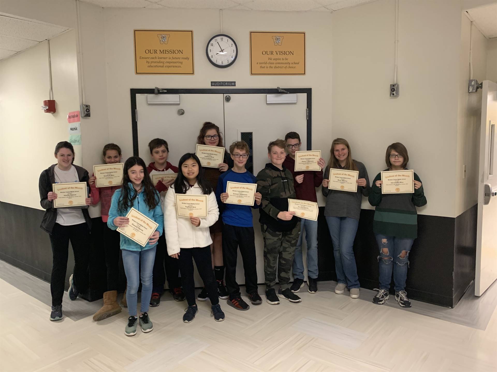 11 students holding certificates in a hallway